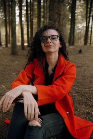 portrait of curly brunette woman in red coat in the parkの写真素材