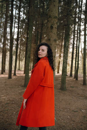 portrait of curly brunette woman in red coat in the parkの写真素材