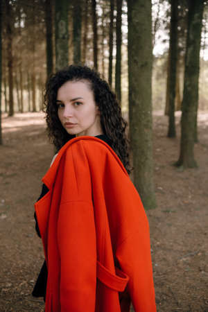 portrait of curly brunette woman in red coat in the parkの写真素材