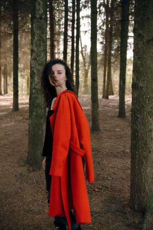 portrait of curly brunette woman in red coat in the parkの写真素材