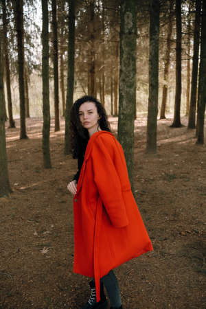 portrait of curly brunette woman in red coat in the parkの写真素材