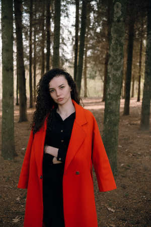 portrait of curly brunette woman in red coat in the parkの写真素材
