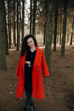 portrait of curly brunette woman in red coat in the parkの写真素材