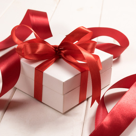 White gift box with red ribbons isolated on white wooden backgroundの写真素材