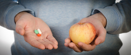 A man holding a fruit and handful of pills. Healthy lifestyle and diet concept.の写真素材