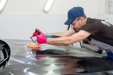A man polishes a black car with a polishing machineの写真素材