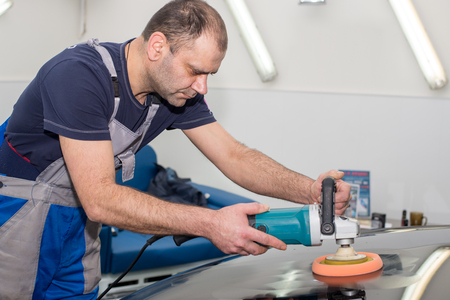 A man polishes a black car with a polishing machineの写真素材