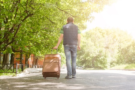 A man traveler with a suitcase walks down the streetの写真素材