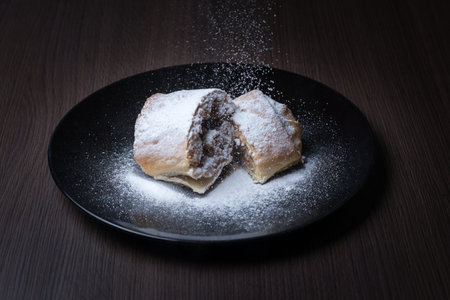 Two pieces of apple strudel on a black plate, top is sprinkled with powdered sugar