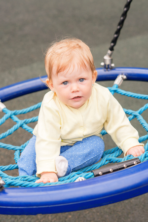 A baby kid is riding on a swing in the autumn in the parkの写真素材
