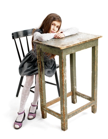 Sad Girl Sitting on Chair and Leaning on Big Table closeup on white backgroundの写真素材