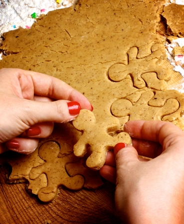 Hands of Women with Red Manicure Making Gingerbread Men with Dough and Flour on Wooden backgroundの写真素材