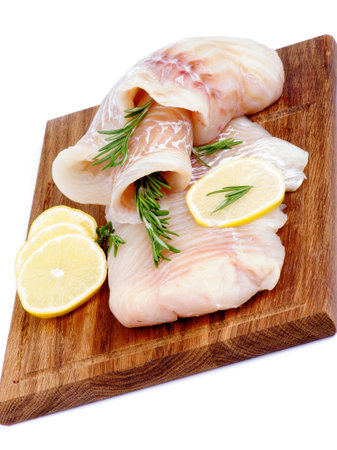 Two Slices of Raw Cod Fish Fillet with Lemon and Rosemary on Wooden Cutting Board isolated on white...