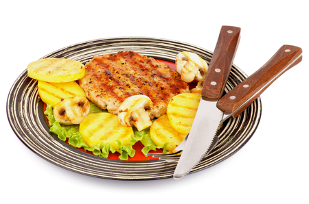 Roasted Turkey Steak Garnished with Grilled Sliced Potato, Portabello Mushrooms, Lettuce on Striped Plate with Fork and Knife isolated on white backgroundの写真素材