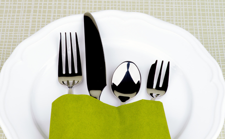 Elegant Table Setting with Fork, Table Knife, Spoon and Dessert Fork into Green Napkin Decorated on White Plate closeup on Checkered background の写真素材