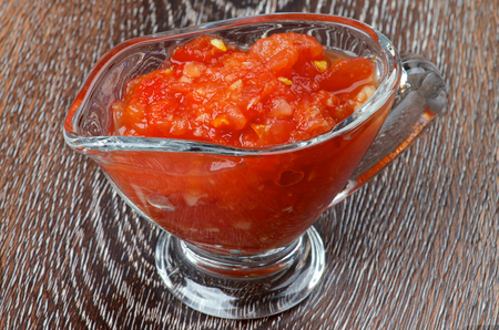 Hot Salsa Sauce in in Glass Gravy Boat isolated on Wooden backgroundの写真素材