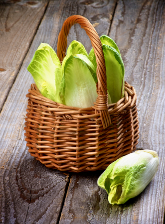 Fresh Crunchy Endive Leaves in Wicker Basket closeup on Rustic Wooden backgroundの写真素材