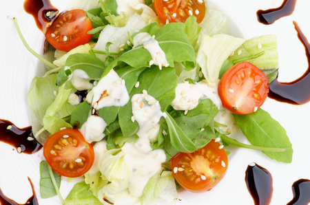 Fresh Greens Salad with Arugula, Lettuce Leafs, Parmesan Cheese, Tomato, Sesame Seeds and Soy Sauce closeup on White Plateの写真素材