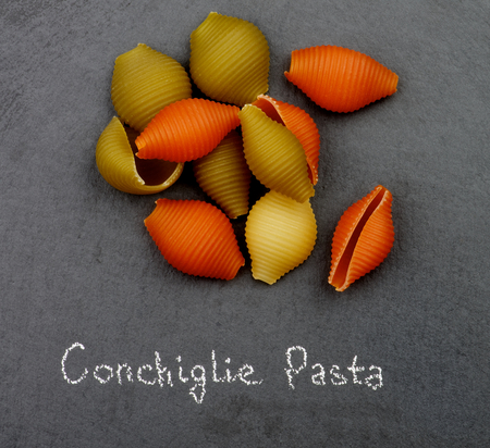 Heap of Raw Conchiglie Tricolore Pasta with Inscription closeup on Black Stone backgroundの写真素材