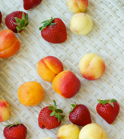 Arrangement of Fresh Ripe Apricots, Strawberries and Peaches closeup on White Wicker background. Top Viewの写真素材
