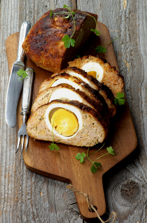 Delicious Homemade Meatloaf Stuffed with Boiled Eggs on Cutting Board with Knife and Fork closeup on Rustic Wooden backgroundの写真素材