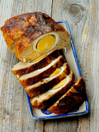 Slices and Half of Delicious Homemade Meatloaf Stuffed with Boiled Eggs on Plate closeup on Rustic Wooden backgroundの写真素材