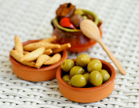 Traditional Spanish Snacks with Green Olives, Bread Sticks and Fried Vegetables in Ceramic Bowls closeup on Wicker background. Focus on Foregroundの写真素材