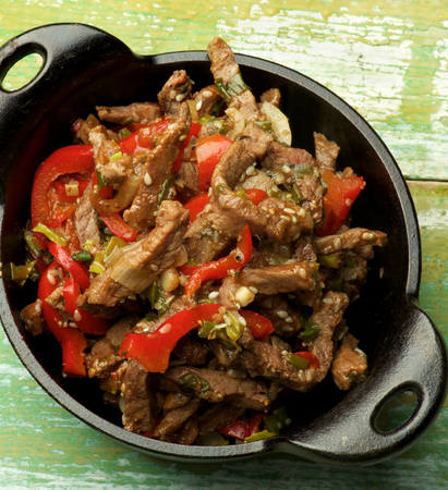 Delicious Beef Stir-fry with Sliced Red Bell Pepper, Leek and Sesame Seeds in Black Cast Iron closeup on Wooden backgroundの写真素材