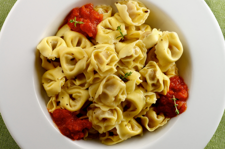 Delicious Meat Cappelletti in with Tomatoes Sauce in White Plate closeup on Green Napkin backgroundの写真素材