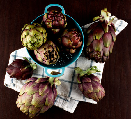 Arrangement of Perfect Raw Artichokes in Blue Colander closeup on Checkered Napkin closeup on Dark Wooden background. Top Viewの写真素材