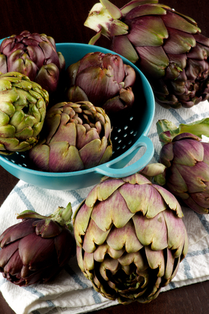 Heap of Perfect Raw Artichokes in Blue Colander on Checkered Napkin closeup on Dark Wooden backgroundの写真素材