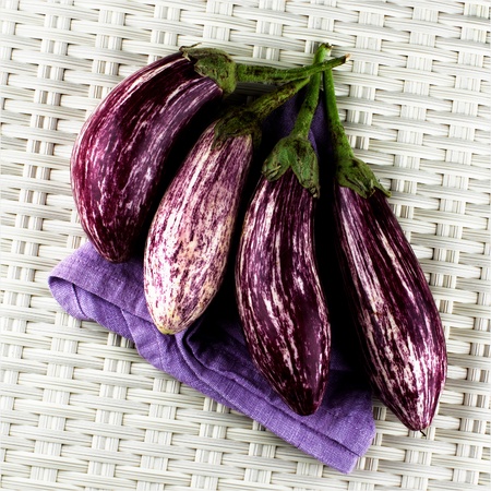 Arrangement of Fresh Raw Striped Eggplants on Purple Napkin closeup on Wicker backgroundの写真素材