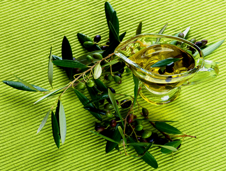 Fresh Olive Oil in Glass Gravy with Raw Green and Black Olives with Leafs on Green Textile background. Top Viewの写真素材