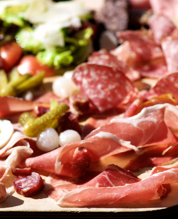 Wooden Plate of Delicious Cold Cuts with Smoked Ham, Cured Sausage, Salami, Marinated Onions and Vegetables closeup Outdoors. Focus on Foregroundの写真素材
