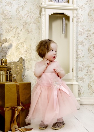 Cute Little Girl in Fluffy Pink Dress near Christmas Gifts under Watch Waiting for Holiday closeupの写真素材