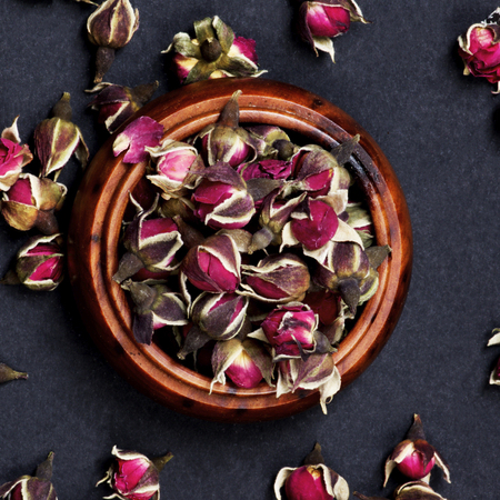 Arrangement of Small Dried Rose Buds Tea in Wooden Jar closeup on Black background. Top Viewの写真素材