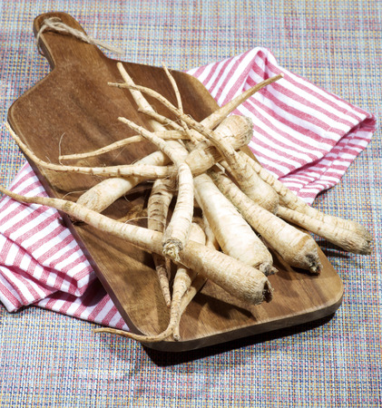 Heap of Fresh Ripe Parsnip Roots on Wooden Cutting Board closeup on Striped Napkinの写真素材
