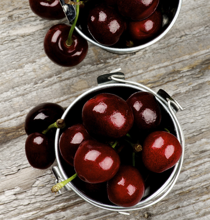 Sweet Dark Red Cherries in Tin Buckets on Rustic Wooden background. Top Viewの写真素材