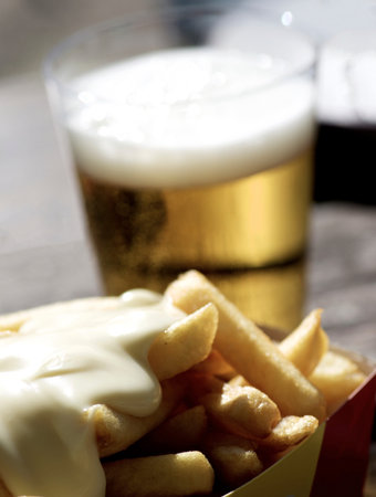 Delicious French Fries with Cheese Sauce on Blurred Glass of Beer closeup on Wooden Table