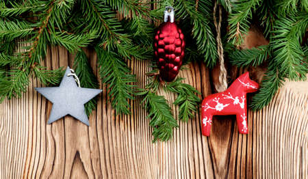 Christmas Decoration with Red Horse, Decorative Cone and Silver Star between Spruce Branch closeup on Wooden backgroundの写真素材