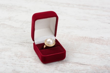 Golden pearl ring in a red gift box on white wooden backgroundの写真素材