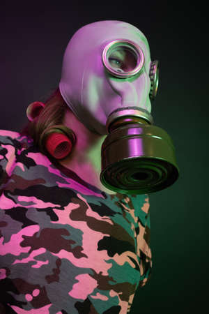 Girl in gas mask and bigodies. Wearing a T-shirt with pink-green camouflage on a dark backgroundの写真素材