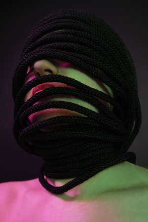 Girl with rope wrapped around her head. Pink-green lightingの写真素材