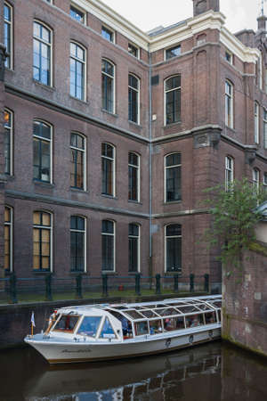 Amsterdam. Netherlands - 06.04.2008. A tourist boat sails along a narrow canal near the University ofのeditorial素材