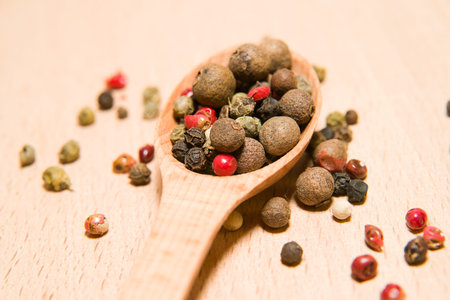 Wooden spoon filled with a mixture of grains of pepper are on a wooden surface