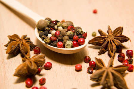 Wooden spoon filled with a mixture of grains of pepper and star anise on a wooden surface