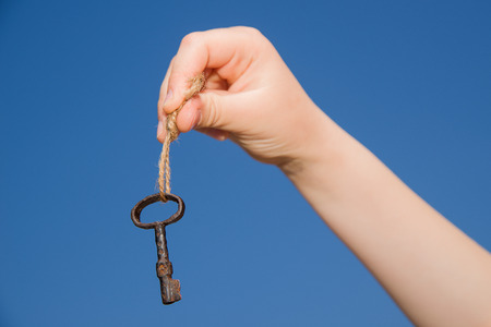 Child hand holding an old key on a string against the skyの写真素材