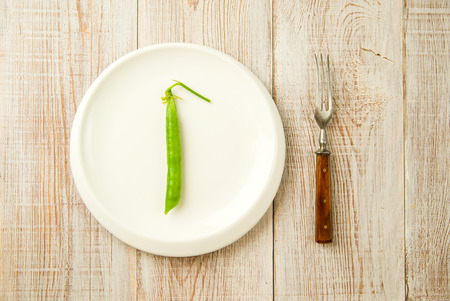 Green pea pod and fork on the white plate.の写真素材
