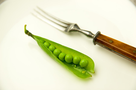 Green pea pod and fork on the white plate.の写真素材