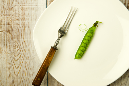 Green pea pod and fork on the white plate.の写真素材